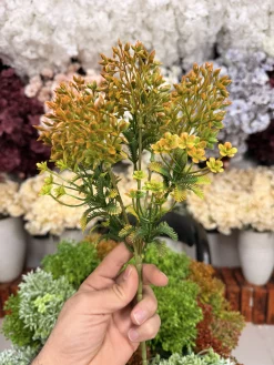 بوته قاصدک مصنوعی سبز فسفری در گلدانی روی نرده یک بالکن آفتابی قرار گرفته است